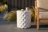 Tortorici antique white faceted concrete side table on dark basalt pavers in an Austin backyard, a charcoal cedar wall and feather grass behind, a mug and a lemon on top (chair and tableware not included)