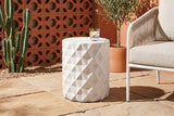 Tortorici faceted concrete side table on sand-coloured pavers in a Palm Springs patio, an orange breeze-block wall and a cactus behind, a glass of iced water on top, a white rope lounge chair beside it (chair and decor not included)