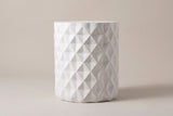 The Tortorici side table seen straight from the side: an upright antique white drum with staggered diamond facets