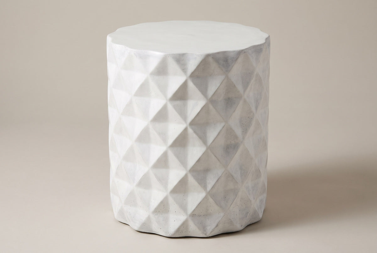 The Tortorici antique white faceted concrete drum side table, three-quarter view on a light studio backdrop