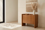 Trani oak veneer accent cabinet with a cream vase of dried pampas and a carved wooden bowl on its tray top, against a pale limestone wall in an Austin living room
