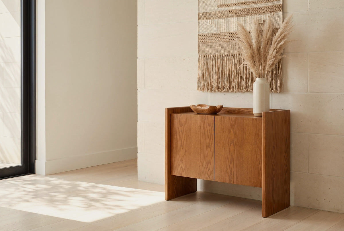 Trani oak veneer accent cabinet with a cream vase of dried pampas and a carved wooden bowl on its tray top, against a pale limestone wall in an Austin living room