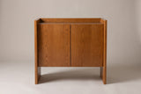 The Trani cabinet in honey oak veneer, front view on a light studio backdrop: two flat doors, a tray top and two slab ends with open floor between them
