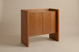 The Trani accent cabinet in honey oak veneer, three-quarter view on a light studio backdrop: two full-height slab ends, a tray top and two flat doors