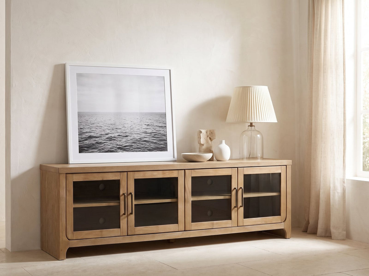 Tremezzo Washed Oak Media Console styled with a leaning print, a lamp and ceramics in a bright plaster room