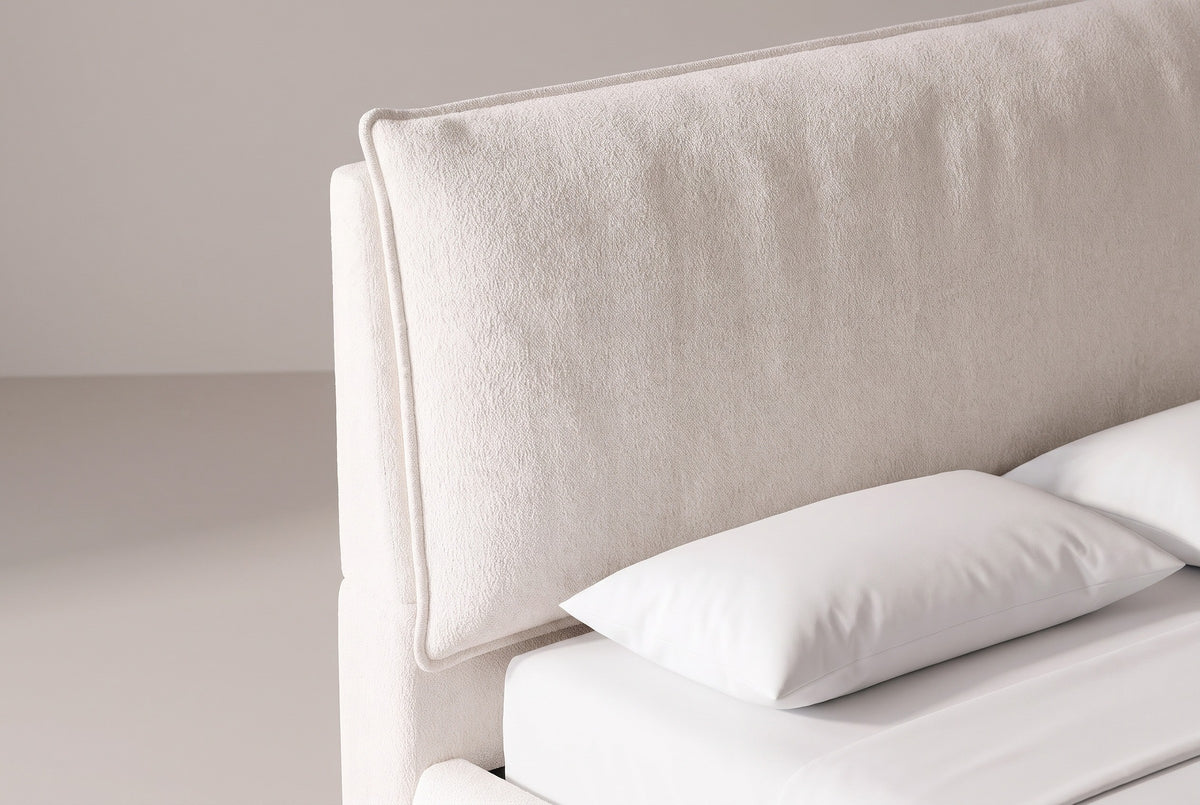 The upper corner of the Trivento headboard: the oversized pillow cushion with its flat flange edge tilted against the plain upholstered panel, above a white pillow