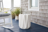 Troina antique white faceted concrete side table on a navy-painted porch floor against silver cedar shingles on the Outer Banks, beside a white rocking chair (chair and carafe not included)