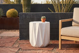 Troina concrete side table on rust-red flagstone in a Tucson desert patio with a charcoal board-formed concrete wall and cactus, beside an oak armchair (chair and plant not included)