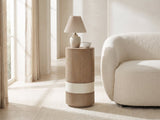 Tuglie Cerused Toffee Drum Side Table with a lamp and a ceramic bowl beside a cream boucle armchair in a bright plaster room