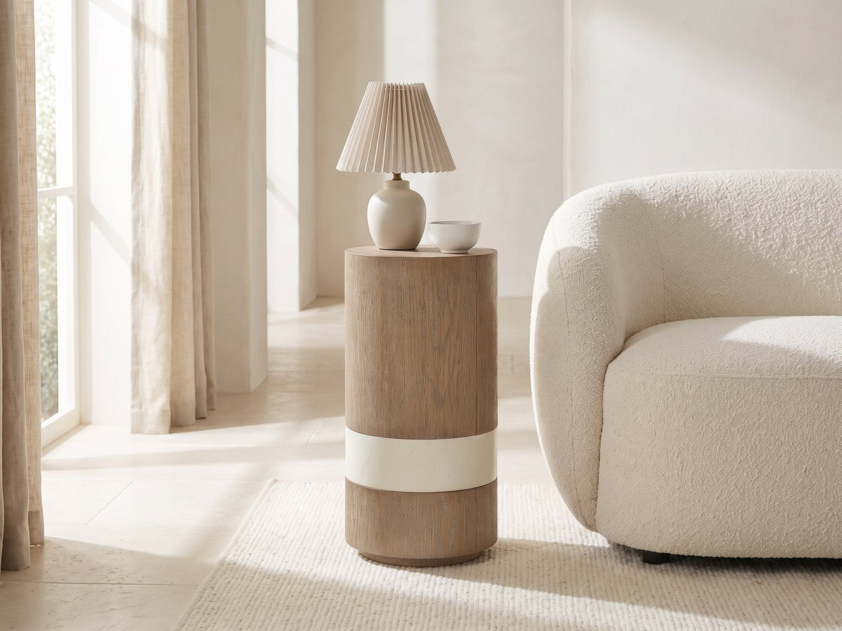 Tuglie Cerused Toffee Drum Side Table with a lamp and a ceramic bowl beside a cream boucle armchair in a bright plaster room