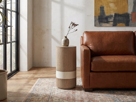 Tuglie Cerused Toffee Drum Side Table beside a leather sofa in an industrial loft