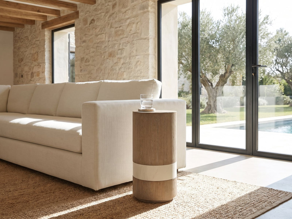 Tuglie Cerused Toffee Drum Side Table beside a linen sofa in a poolside villa