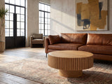 Udine Natural Wood Veneer Fluted Pedestal Coffee Table on a vintage rug in front of a leather sofa in an industrial loft
