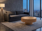Udine Natural Wood Veneer Fluted Pedestal Coffee Table on a wool rug in front of a velvet sofa in a city penthouse at blue hour