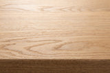 Close-up of the solid red oak on the Umbertide bench: light honey-beige open grain running to the eased edge of the top