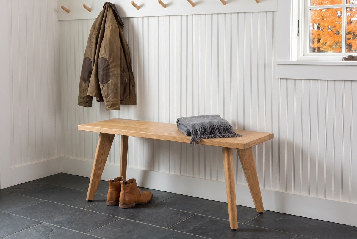 Umbertide bench against white beadboard in a Vermont farmhouse mudroom with a slate floor, wooden pegs and autumn trees outside