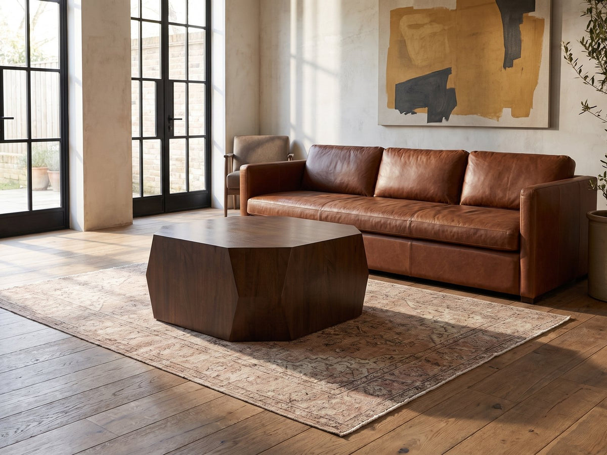 Urbino Acacia Veneer Faceted Coffee Table seen from the side, on a vintage rug in front of a leather sofa in an industrial loft