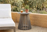 Valderice slatted acacia side table on a decomposed-granite terrace in Ojai, California, a rammed-earth wall, olive trees and lavender behind, a white lounge chair beside it (chair, glass and plant not included)