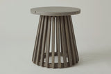 The Valderice side table seen from the front: the round top over a base of straight acacia slats flaring out to the floor ring