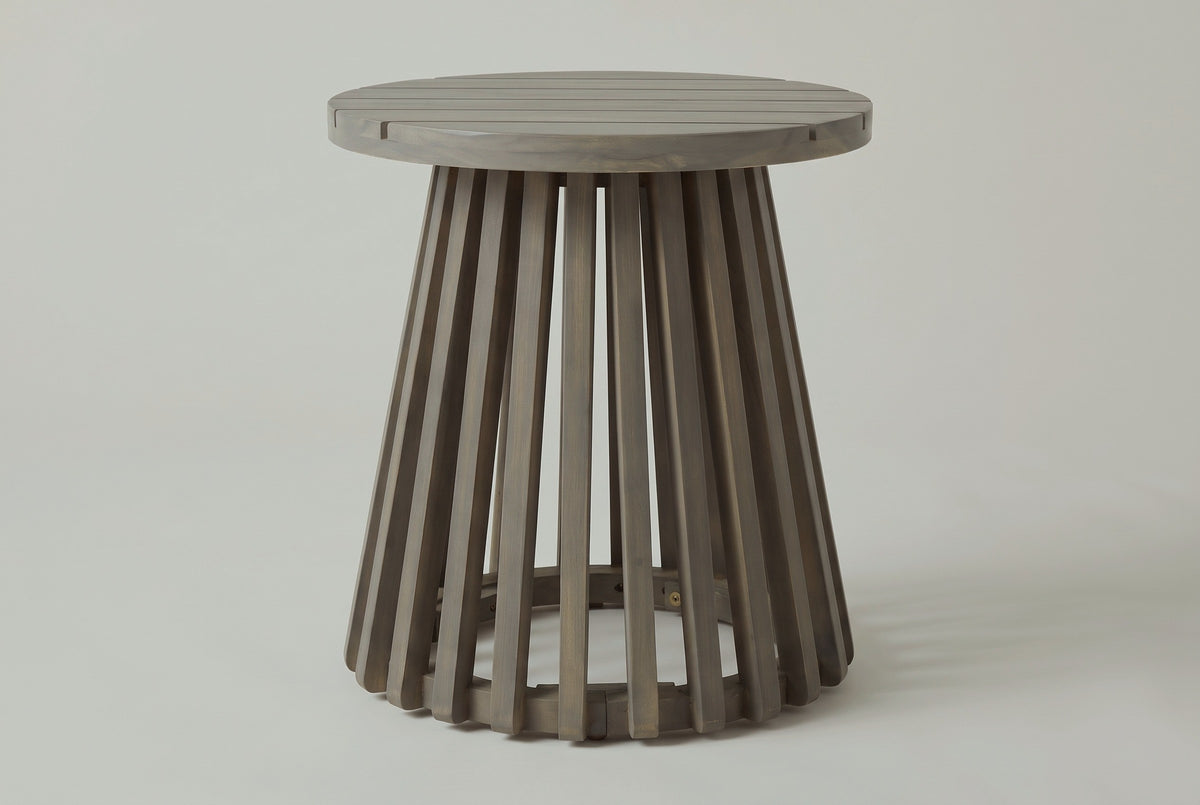 The Valderice side table seen from the front: the round top over a base of straight acacia slats flaring out to the floor ring