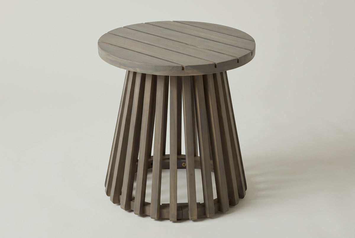 The Valderice round acacia side table in weathered grey, three-quarter view on a light studio backdrop