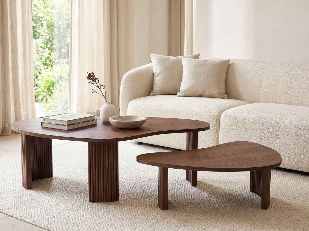 Valenza 50-Inch Freeform Walnut-Stained Veneer Nesting Coffee Tables, Set of 2 styled with books, a vase and a stone bowl in front of a cream sofa in a bright plaster room