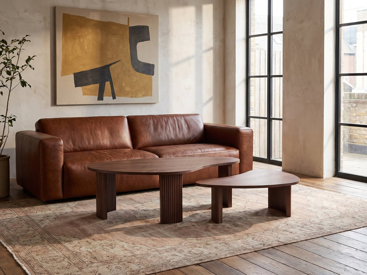 Valenza 50-Inch Freeform Walnut-Stained Veneer Nesting Coffee Tables, Set of 2 on a vintage rug in front of a leather sofa in an industrial loft