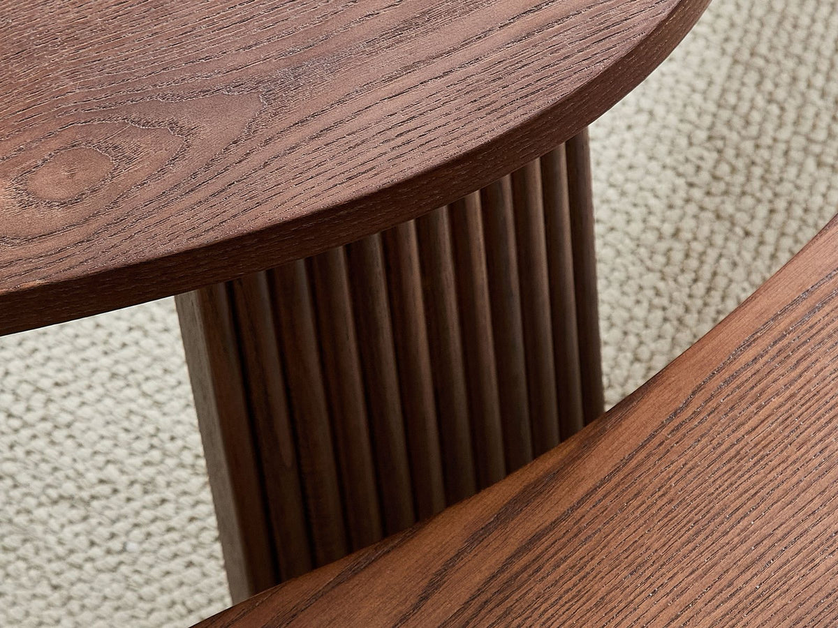 Close-up of the Valenza 50-Inch Freeform Walnut-Stained Veneer Nesting Coffee Tables, Set of 2: a reeded curved-panel leg under the thin veneered top edge