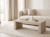Varallo Reclaimed Pine Waterfall Coffee Table styled with books, a vase and a stone bowl in front of a cream sofa in a bright plaster room