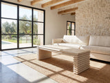 Varallo Reclaimed Pine Waterfall Coffee Table seen from the side, on a jute rug in front of a linen sofa in a poolside villa