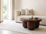 Bolgheri Sculpted Mango Coffee Table styled with books, a vase and a stone bowl in front of a cream sofa in a bright plaster room