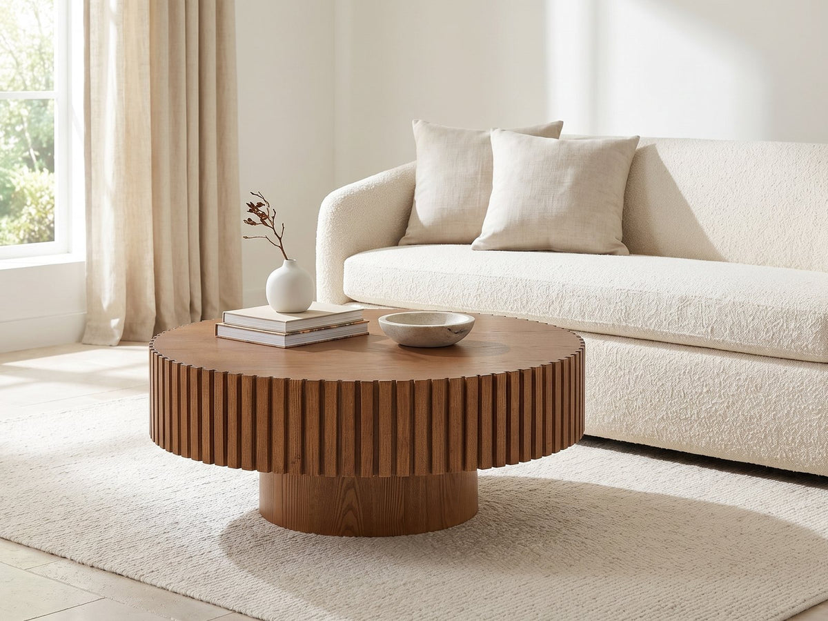 Vernazza Wood Veneer Fluted Pedestal Coffee Table styled with books, a vase and a stone bowl in front of a cream sofa in a bright plaster room