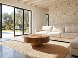 Vernazza Wood Veneer Fluted Pedestal Coffee Table seen from the side, on a jute rug in front of a linen sofa in a poolside villa