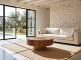 Vernazza Wood Veneer Fluted Pedestal Coffee Table on a jute rug in front of a linen sofa in a poolside villa