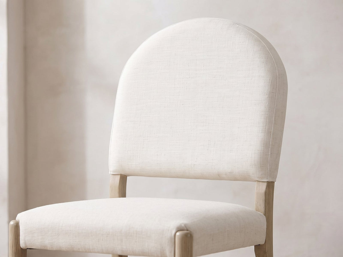 Close-up of the Veroli 47-Inch Round Fluted Pedestal Dining Set with 4 Chairs: the round-arched upholstered back and padded seat of a chair in cream woven fabric