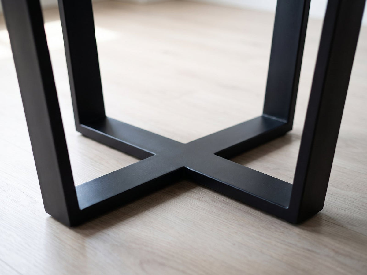 Close-up of the Verzino 47-Inch Round Black Acacia Sunburst Dining Table: the black iron base: two U-shaped frames crossing in a flat X on the floor
