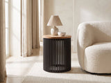 Viggiano Mango and Black Metal Drum Side Table with a lamp and a ceramic bowl beside a cream boucle armchair in a bright plaster room
