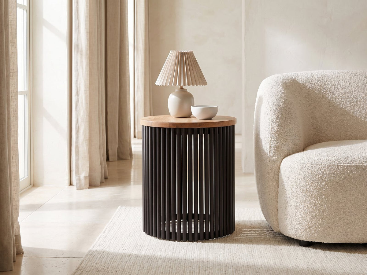 Viggiano Mango and Black Metal Drum Side Table with a lamp and a ceramic bowl beside a cream boucle armchair in a bright plaster room