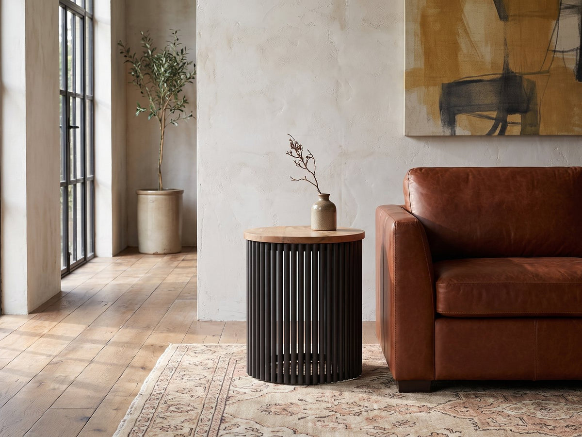 Viggiano Mango and Black Metal Drum Side Table beside a leather sofa in an industrial loft