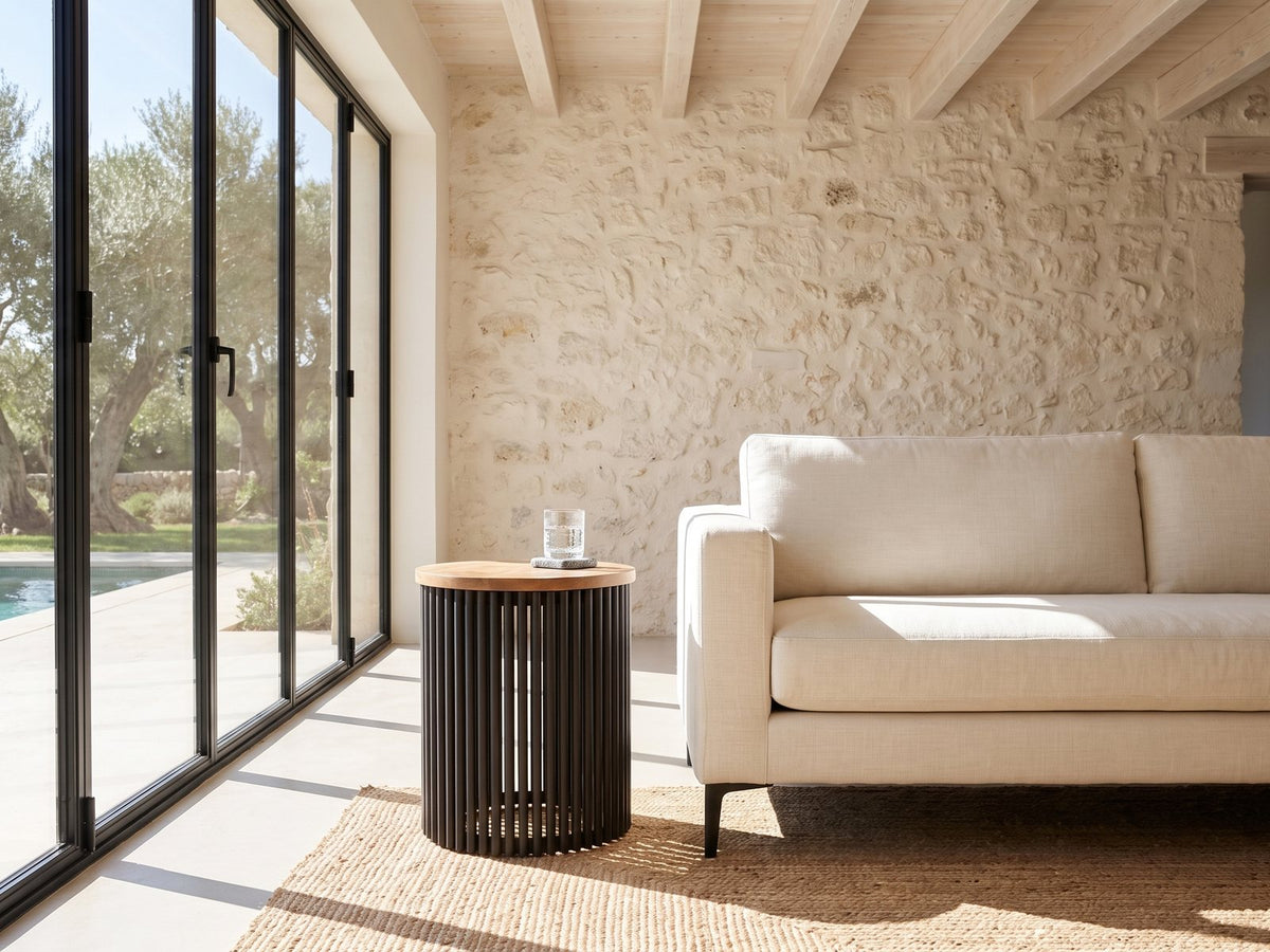 Viggiano Mango and Black Metal Drum Side Table beside a linen sofa in a poolside villa