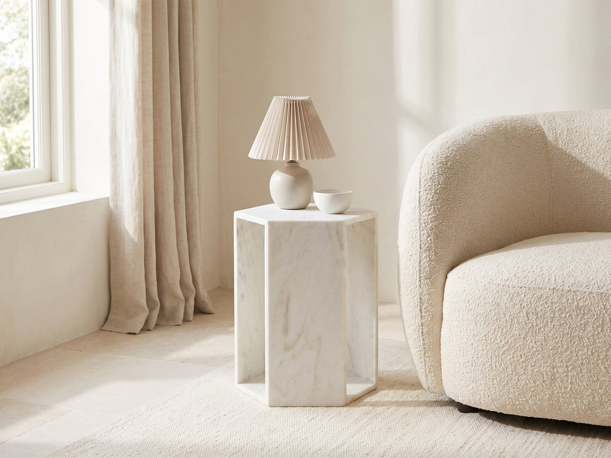 Vitozza White Marble Hexagon Side Table with a lamp and a ceramic bowl beside a cream boucle armchair in a bright plaster room