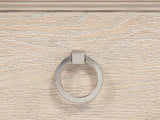 Close-up of the Vittorio 62-Inch Washed Oak 6-Drawer Dresser: a polished nickel ring pull on a washed oak drawer, under the stepped mitred moulding