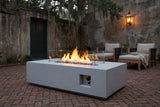 Vulcano concrete fire pit table lit at dusk on a herringbone brick courtyard in Savannah, Georgia, with an old mossy stucco wall, a lantern and live oaks behind (chairs not included)