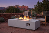Vulcano concrete fire pit table lit at dusk on a red sandstone flagstone patio in Sedona, Arizona, with a dry-stacked red stone wall, agaves and red rock buttes behind (chairs not included)