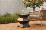 Zafferana charcoal bronze geometric side table on an ipe wood deck in Dallas, a board-formed concrete wall, grasses and a rope lounge chair behind (chair and carafe not included)