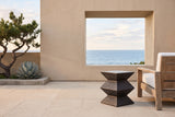 Zafferana charcoal bronze geometric concrete side table on limestone pavers on a La Jolla terrace, a sand stucco wall framing the Pacific and a teak lounge chair behind (chair not included)