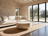Zagarolo Faux Travertine Round Drum Coffee Table on a jute rug in front of a linen sofa in a poolside villa