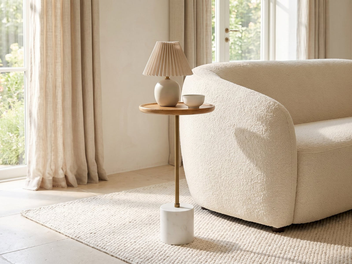 Zollino Mango and Marble Pedestal Side Table with a lamp and a ceramic bowl beside a cream boucle armchair in a bright plaster room